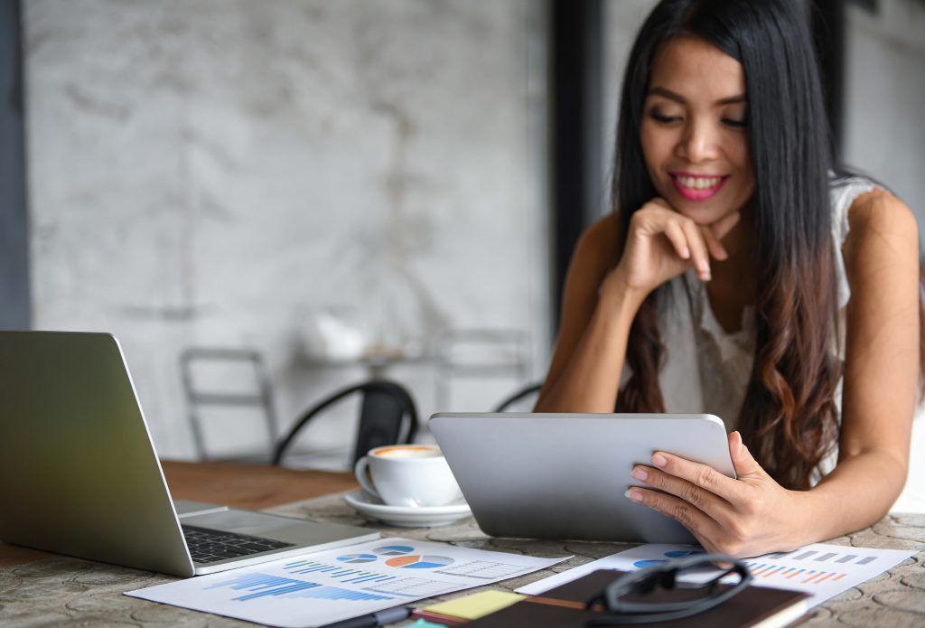 Young woman using a tablet during leisure. Graphs, documents placed on the table. Creating a profitable website.