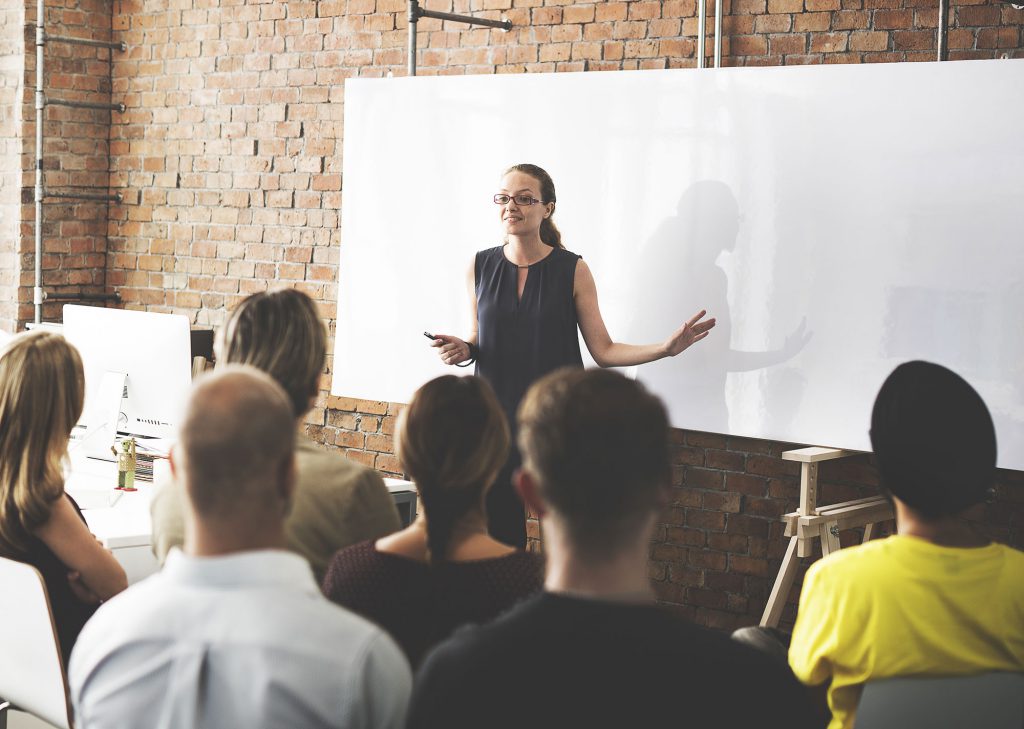 A woman standing in front of a whiteboard presenting to a group